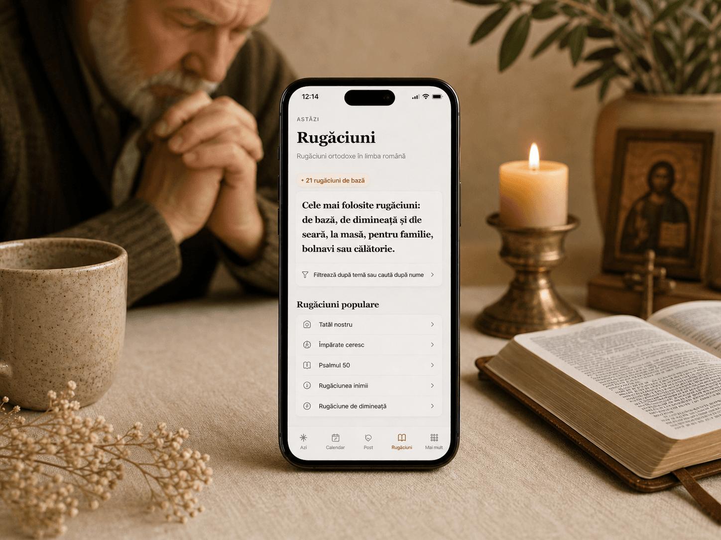 Telefon cu pagina „Rugăciuni” lângă o Biblie deschisă, lumânare, ceașcă de ceai și metanier.